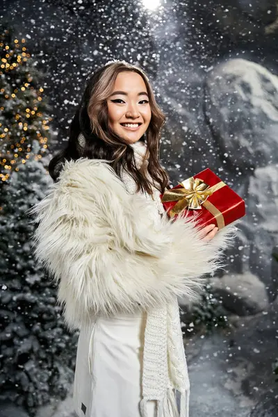 A delighted young woman enjoys the festive spirit while holding a red gift adorned with gold. — Stock Photo