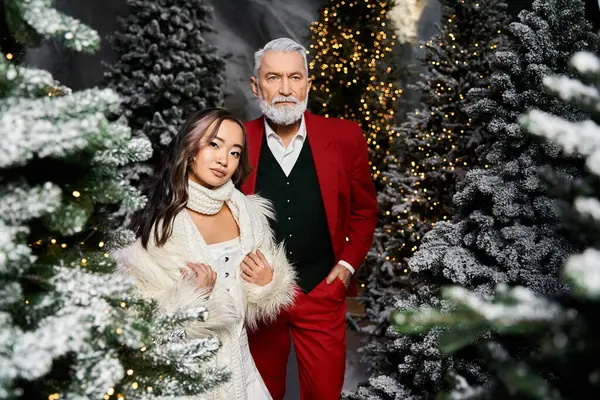 An elegant couple poses in a festive winter wonderland adorned with snow and lights. — Stock Photo