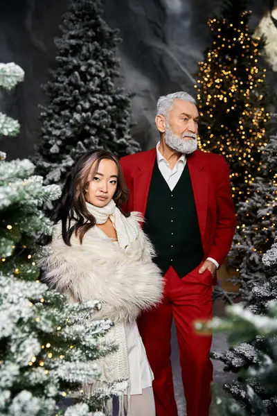A couple in elegant winter clothing poses together, surrounded by decorated Christmas trees. — Stock Photo
