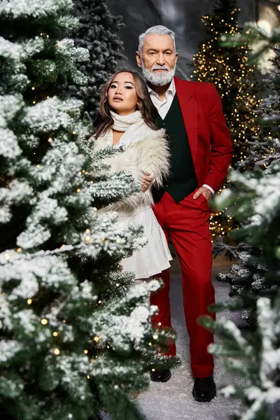 A stylish pair stands together surrounded by decorated trees, celebrating the festive spirit. — Stock Photo