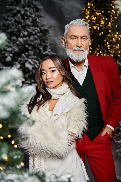 Two elegantly dressed individuals pose together, surrounded by festive decorations and trees. — Stock Photo