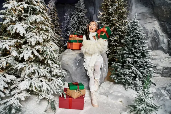 A person joyfully poses with colorful gifts amidst a serene snowy landscape filled with pine trees. — Stock Photo