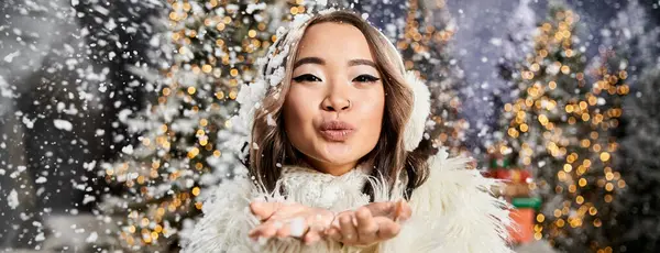 Una persona gioiosa soffia neve nell'aria tra scintillanti decorazioni natalizie durante l'inverno. — Foto stock