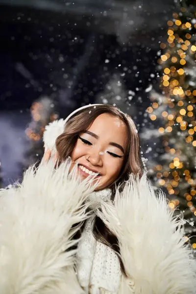 A cheerful individual enjoys the snowfall amidst vibrant Christmas lights and decorations. — Stock Photo