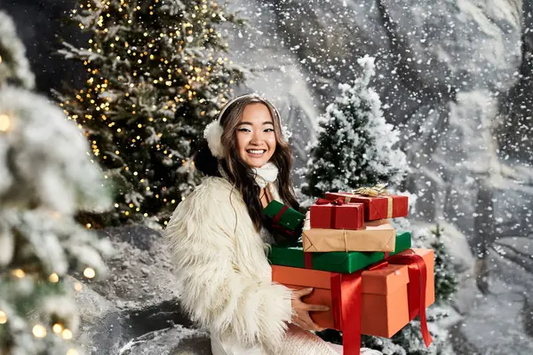 A cheerful young woman carries festive presents against a winter wonderland backdrop. — Stock Photo