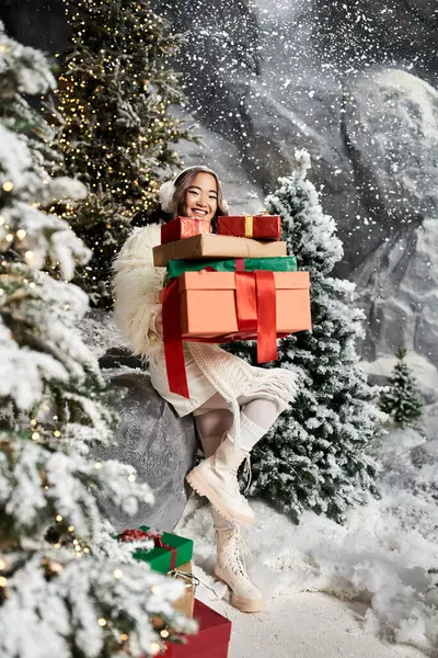 Una persona alegre rodeada de árboles cubiertos de nieve, sosteniendo alegremente regalos envueltos durante la Navidad. - foto de stock