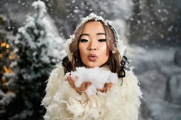 Una giovane donna gioca in un paesaggio innevato, soffiando ondate di neve in aria sorridendo. — Foto stock