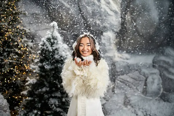 Snowflakes gently fall around a smiling woman dressed in white amid a magical Christmas backdrop. — Stock Photo