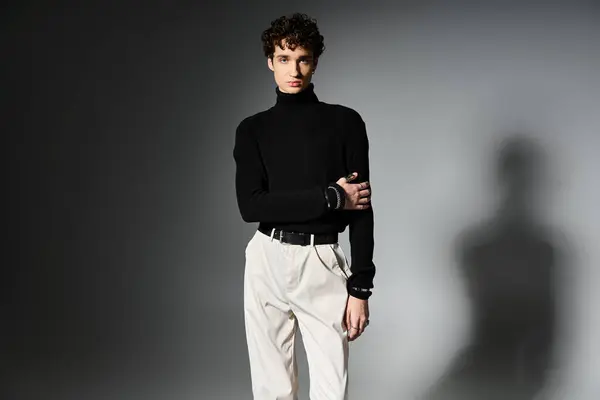 The young man sports curly hair and a stylish black turtleneck against a dark background. — Stock Photo