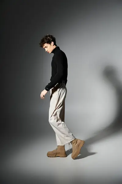 A fashionable young man stands elegantly, showcasing his black turtleneck and light trousers in a studio setting. — Stock Photo