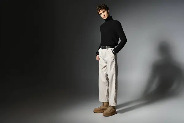 A handsome young man with curly hair showcases a modern outfit on a dramatic dark grey background. — Stock Photo