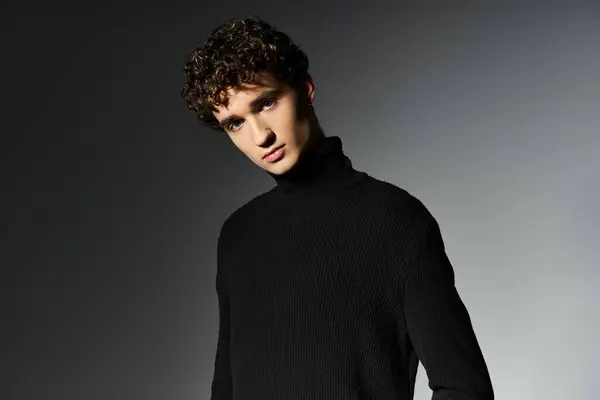 A young man with curly hair showcases his fashionable black turtleneck, exuding confidence in a moody setting. — Stock Photo