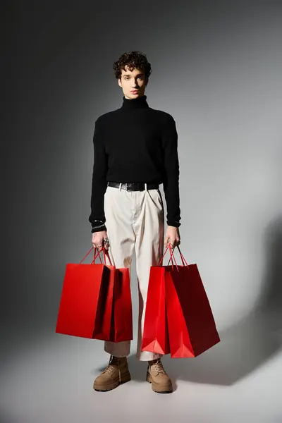 Um jovem elegante com cabelo encaracolado mantém sacos de compras brilhantes, incorporando a emoção da Black Friday. — Fotografia de Stock