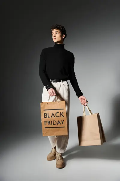 Um jovem com cabelo encaracolado mantém sacos de compras, mostrando sua emoção para negócios Black Friday dentro de casa. — Fotografia de Stock