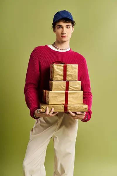 A stylish young man with curly hair proudly presents colorful Christmas gifts in a bright studio setting. — Stock Photo