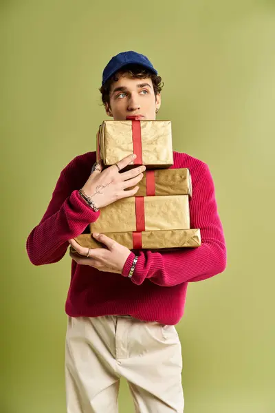 A charming young man with curly hair embraces beautifully wrapped Christmas gifts in a studio. — Stock Photo