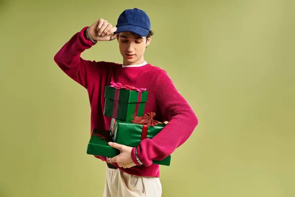 A young man with curly hair showcases Christmas gifts in a vibrant studio environment. — Stock Photo