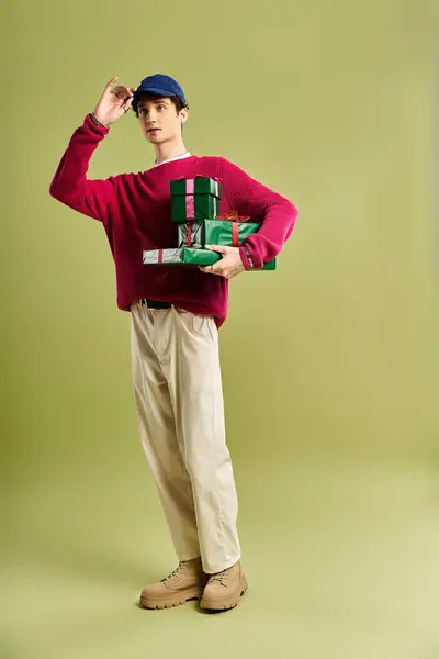 A stylish young man with curly hair poses with Christmas presents, exuding holiday cheer in a studio. — Stock Photo
