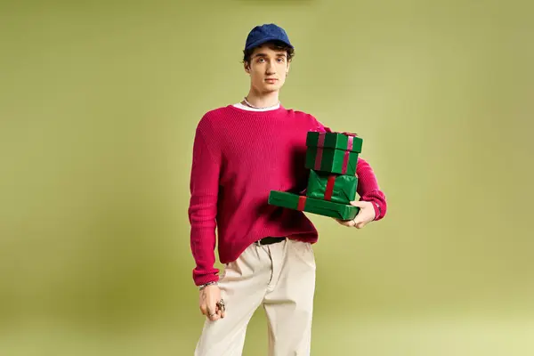 A handsome young man is delightedly presenting colorful Christmas gifts in a vibrant studio. — Stock Photo