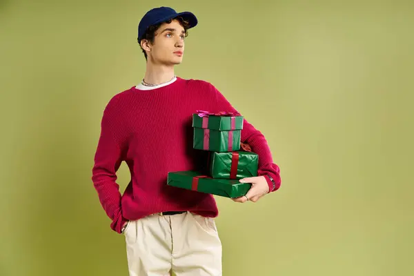 A stylish young man embraces the holiday spirit while holding colorful presents in a cheerful studio. — Stock Photo