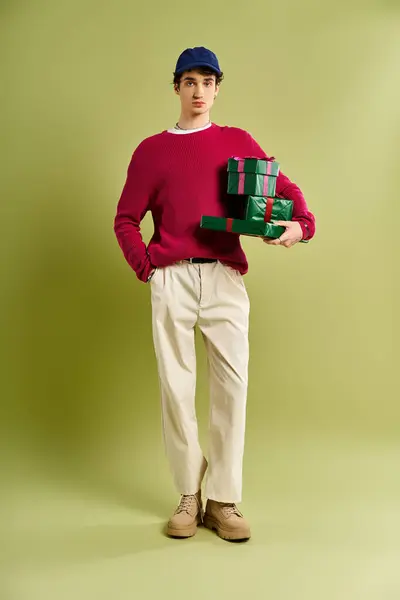 Dans un studio vibrant, un beau jeune homme aux cheveux bouclés présente joyeusement des cadeaux de Noël enveloppés de vert. — Photo de stock