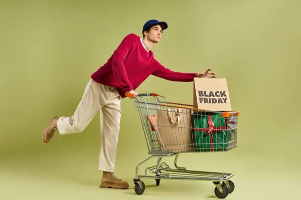 Um jovem elegante detém sacos de compras e um carrinho, abraçando a emoção das vendas Black Friday. — Fotografia de Stock