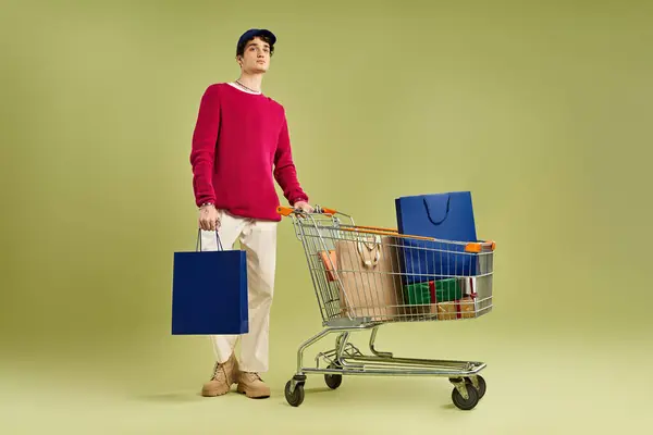 A young man with curly hair holds shopping bags, excited for Black Friday deals in a vibrant studio. — Stock Photo