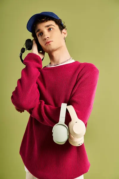 Un giovane uomo affascina con la sua posa affascinante, indossa un maglione rosa e tiene le cuffie su uno sfondo pastello. — Foto stock