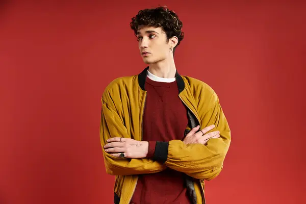 A handsome young man with curly hair stands with crossed arms, looking away in a vibrant yellow jacket. — Stock Photo