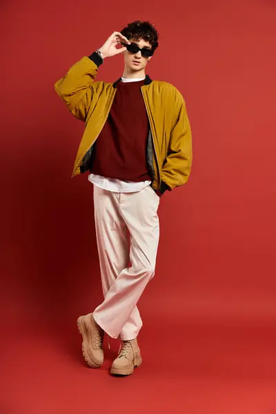 A young man confidently poses in a yellow jacket against a bright red background, showcasing his style. — Stock Photo