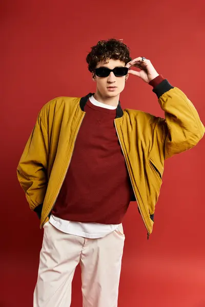 A stylish young man with curly hair showcases his bold fashion sense in a yellow jacket and sunglasses. — Stock Photo