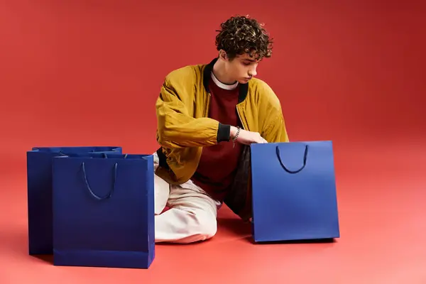 A fashionable young man with curly hair enjoys his Black Friday shopping experience surrounded by bags. — Stock Photo
