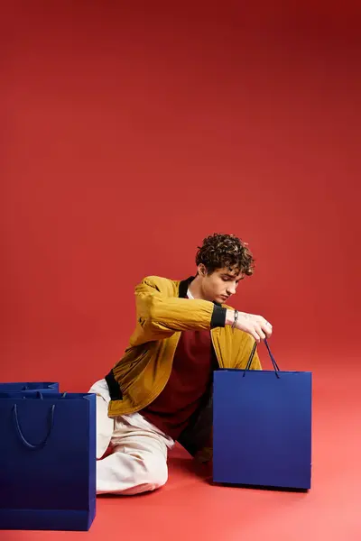 Um jovem bonito examina seus sacos de compras com emoção após as vendas da Black Friday em um estúdio. — Fotografia de Stock