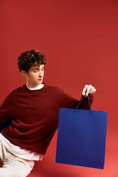 A young man with curly hair showcases colorful shopping bags, celebrating Black Friday in a lively studio setting. — Stock Photo