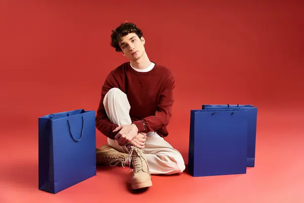 Um jovem elegante com cabelo encaracolado senta-se entre sacos de compras depois de uma diversão Black Friday shopping spree. — Fotografia de Stock