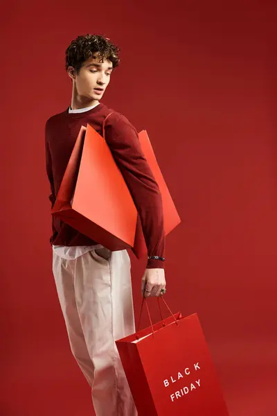 Um jovem elegante mantém sacos de compras festivas, comemorando suas compras bem sucedidas na Black Friday. — Fotografia de Stock