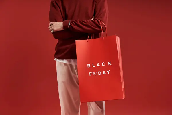Um jovem com cabelo encaracolado segura sacos de compras, comemorando a emoção da Black Friday em um estúdio. — Fotografia de Stock
