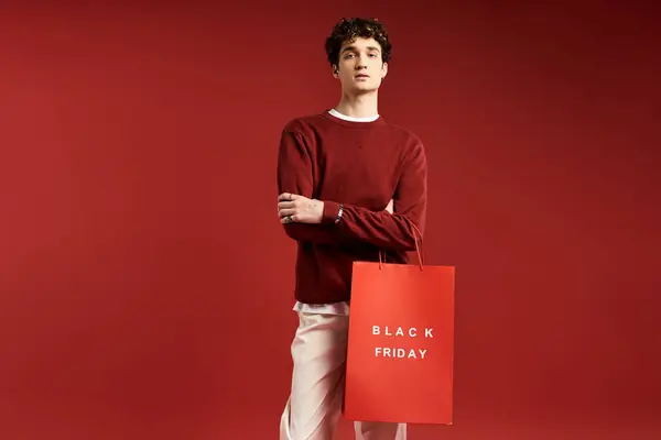 A trendy young man showcases his stylish look while holding shopping bags during Black Friday in a studio. — Stock Photo