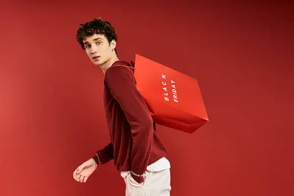 Um jovem bonito com cabelo encaracolado carrega sacos de compras coloridos enquanto celebra a Black Friday em grande estilo. — Fotografia de Stock