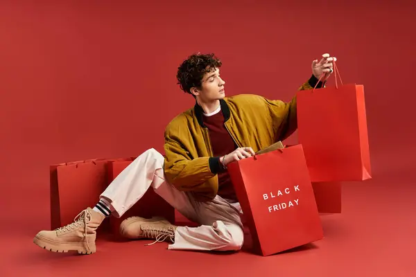 Um jovem elegante mantém vibrantes sacos de compras, comemorando Black Friday em um cenário de estúdio animado. — Fotografia de Stock