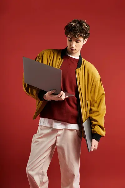 Ein gutaussehender junger Mann in einer stylischen gelben Jacke steht mit einem Laptop bereit und strahlt Kreativität und Charme aus.. — Stockfoto