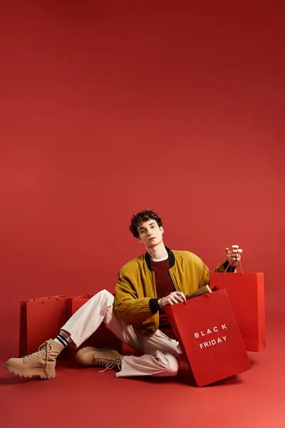 Um jovem bonito com cabelo encaracolado gosta de fazer compras, orgulhosamente segurando sacos em um cenário de estúdio ousado. — Fotografia de Stock