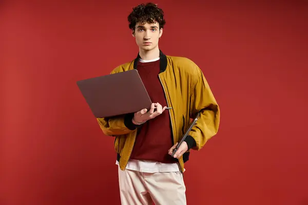 A handsome man with curly hair poses confidently in a yellow jacket while holding a laptop and tablet. — Stock Photo