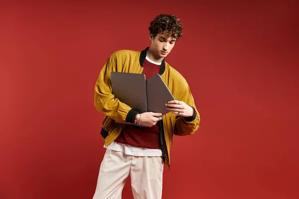A handsome young man with curly hair confidently poses in a striking yellow jacket on a bold red backdrop. — Stock Photo