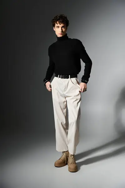 A fashionable young man stands confidently, showcasing his curly hairstyle and chic outfit against a dark backdrop. — Stock Photo