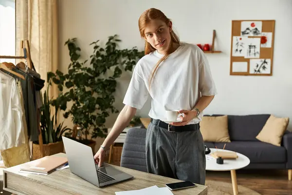 A focused young man engages with his laptop while enjoying a beverage in a cozy space. — Stock Photo