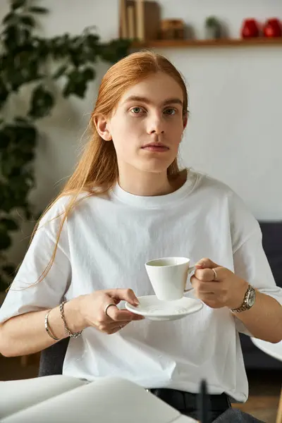 The young man with long hair sits quietly, savoring his coffee. — Stock Photo