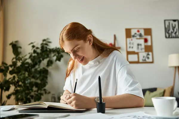 A cheerful young man writes enthusiastically in his notebook at a stylish workspace. — Stock Photo