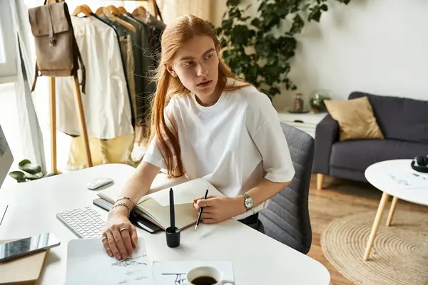Un joven enfocado esboza ideas mientras está sentado en un espacio de trabajo moderno adornado con vegetación. - foto de stock