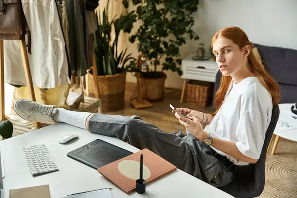 Der junge Mann sitzt entspannt an seinem Schreibtisch, kreativ mit seinem Handy beschäftigt. — Stockfoto